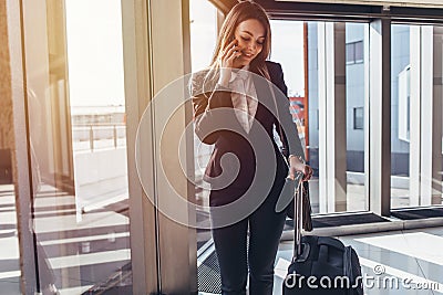 Smiling elegant woman walking with her baggage in airport talking on smartphone Stock Photo