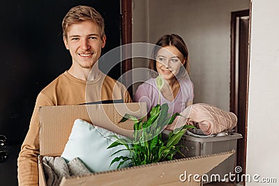 Smiling energetic students teenagers man, woman hold carton box with flower and clothes. Changeover new university room Stock Photo