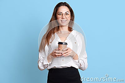 Smiling energetic young girl enjoys drinking hot coffee, holds paper cup in hands, poses, wears formal black skirt and white Stock Photo