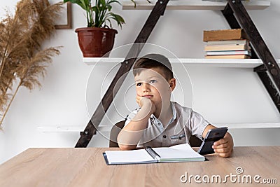 smiling european boy with a smartphone sitting at a table resting from lessons. A student at recess is dreaming and Stock Photo