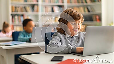 Smiling european schoolboy sitting at desk in front of laptop in classroom, typing or doing homework online, panorama Stock Photo