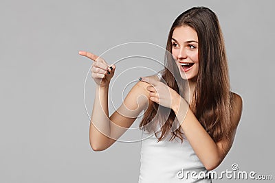 Smiling excited woman showing finger on copy space for product or text, isolated over grey background Stock Photo