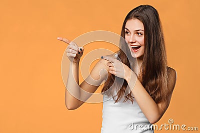 Smiling excited woman showing finger on copy space for product or text, isolated over orange background Stock Photo