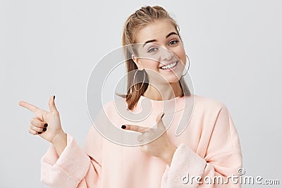 Smiling fair-haired young woman in pink sweatshirt pointing at copy space for your advertisment or text. Positive girl Stock Photo