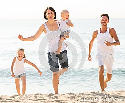 Smiling family of four running on sandy beach Stock Photo