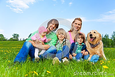 Smiling family sitting on green grass with dog Stock Photo