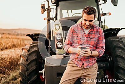 Portrait of smiling farmer using smartphone and tractor at harvesting. Modern agriculture with technology and machinery concept Stock Photo