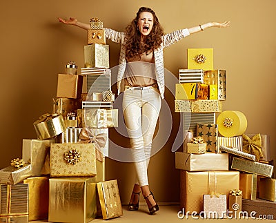 Smiling fashion-monger among 2 piles of golden gifts rejoicing Stock Photo