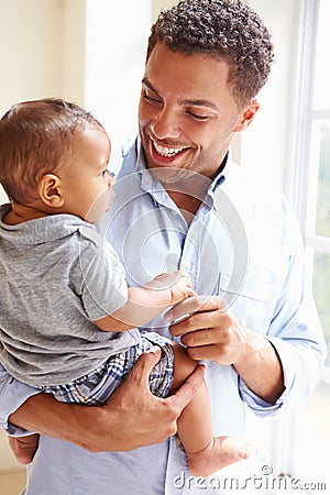 Smiling Father Standing By Window With Baby Son At Home Stock Photo