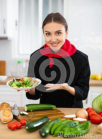 Smiling female chef in black uniform offering plate of vegetable salad Stock Photo