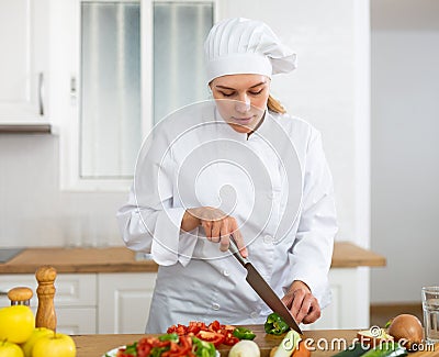 Smiling female chef in white uniform preparing vegetable salad in private kitchen Stock Photo