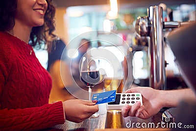 Smiling Female Customer In Bar Making Contactless Payment With Card For Drinks To Male Bartender Editorial Stock Photo