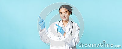 Smiling female doctor, physican in medical uniform and sterile gloves, pointing fingers left at promo, clinic logo Stock Photo