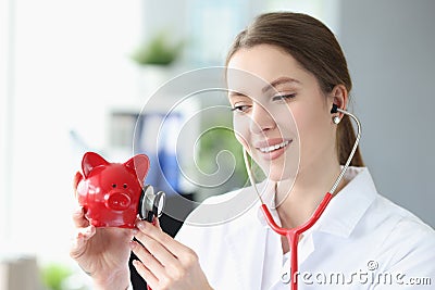 Smiling female doctor stethoscope listens to piggy bank piggy bank Stock Photo