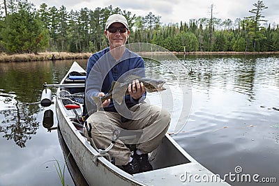 Smiling fisherman sitting in a canoe on a Minnesota lake holds up a walleye Stock Photo