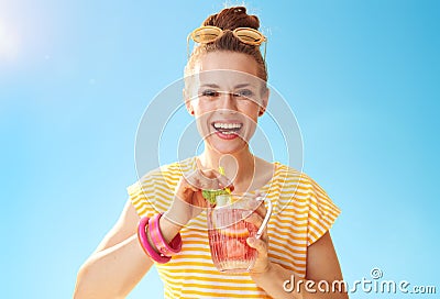 Smiling fit woman against blue sky drinking refreshing cocktail Stock Photo