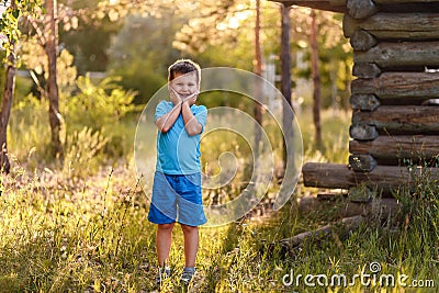 A smiling five-year-old boy in blue clothes stands tall in the Park on a natural background in the summer in the contra sunset Stock Photo