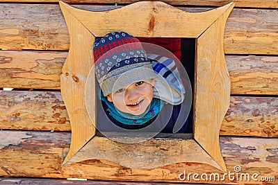 Smiling five-year-old boy boy looks out the window of the house. children`s wooden house on the Playground Stock Photo