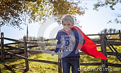 Smiling five year old boy running with red cape outside Stock Photo