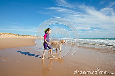 Smiling little girl walking with a dog on the shore of beach Stock Photo