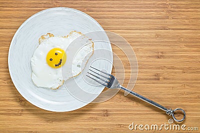 Smiling fried egg lying on a wooden cutting board with morning inscription near it. Classic Breakfast concept. Stock Photo