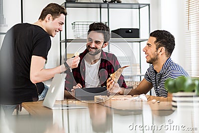 Smiling friends eating pizza and talking about digital cryptocurrency Stock Photo