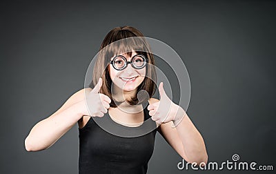 Smiling geek girl in glasses with thumbs up. Happy winner nerd woman. Stock Photo