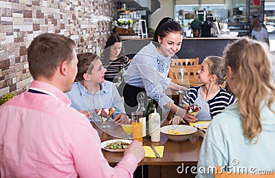 Smiling girl is bringing delicious dessert to young visitors Stock Photo