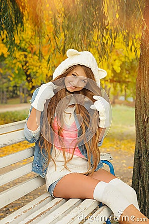 Smiling girl dressed in a cute knitted white bear hat in autumn park. Stock Photo