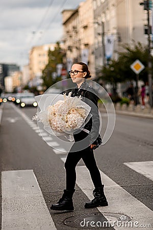 Smiling girl going on the street with a fluffy bouquet of soft flowers in wrapper Stock Photo