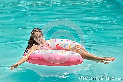 Smiling girl have fun floating on inflatable donut in blue swimming pool Stock Photo