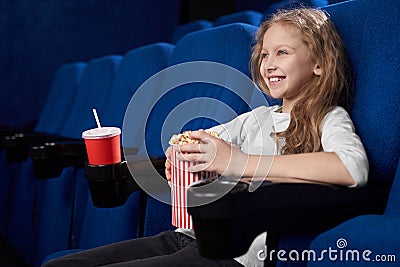 Smiling girl holding popcorn bucket, sitting in cinema. Stock Photo