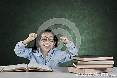 Smiling girl lifting hands with books in classroom Stock Photo