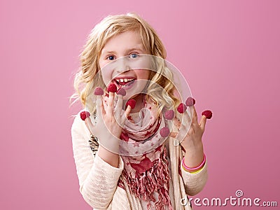 Smiling girl on pink background eating raspberries on fingers Stock Photo
