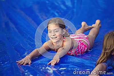 Smiling girl sliding down an outdoor slip and slide Stock Photo