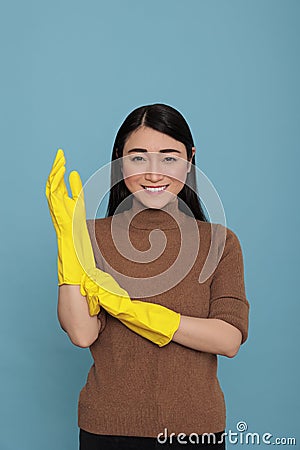 Smiling glad and delighted asian housemaid putting yellow rubber gloves on hand Stock Photo