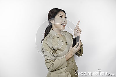 Smiling government worker woman holding her smartphone and pointing to copy space above her. PNS wearing khaki uniform Stock Photo
