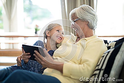 Smiling granddaughter and grandmother using digital tablet on sofa Stock Photo