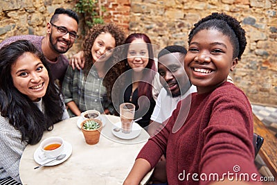 Diverse young friends taking selfies together in a cafe courtyard Stock Photo