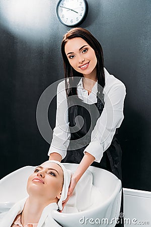 smiling hairdresser drying washed customer hair with towel and looking Stock Photo