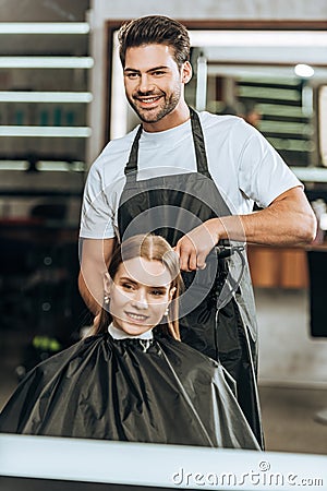 Smiling hairstylist using hair straightener and happy girl looking at mirror Stock Photo