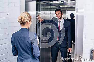 Businessman holding elevator door for woman Stock Photo