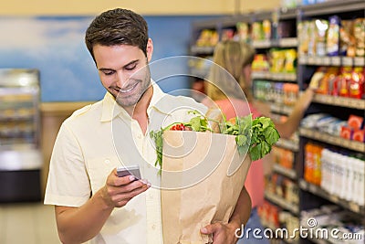 Smiling handsome man buying food products and using his smartphone Stock Photo
