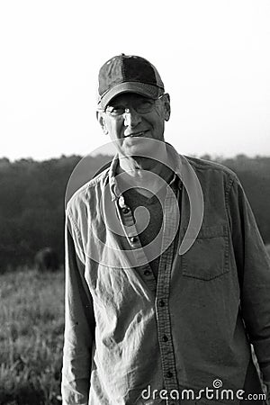 Smiling handsome older Caucasian man with glasses in farm field with trees Editorial Stock Photo