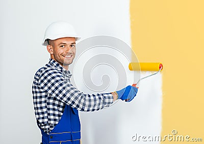 Smiling handsome painter painting the wall in beige Stock Photo