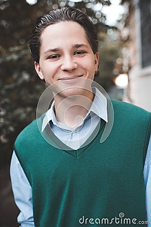 Smiling handsome teen boy student 17-18 year old wear knit vest and shirt outdoors. Happy teenager outdoor on city street. Stock Photo