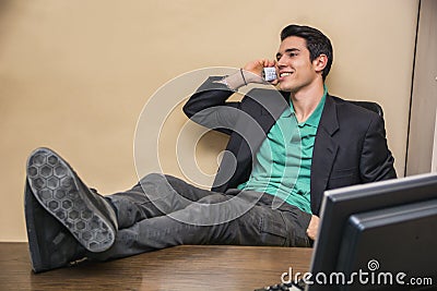 Smiling handsome young businessman at desk on phone Stock Photo