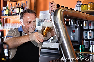 Barman is pouring unbottled beer with foam for client in the bar. Stock Photo