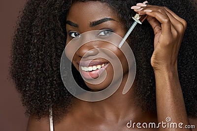 Smiling happy young African black woman applying serum oil on facial skin. Stock Photo