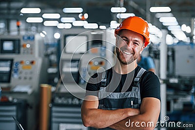 Smiling and happy employee. Portrait of industrial worker indoors in factory. Young technician with orange hard hat Stock Photo